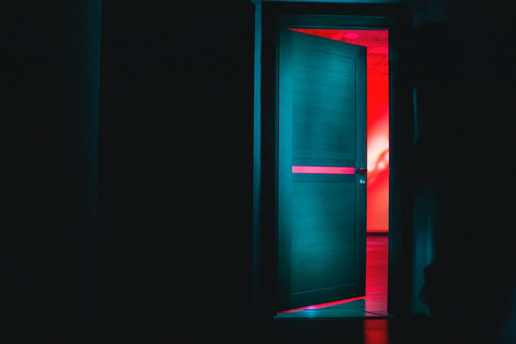 Puerta blanca de madera en la oscuridad con una luz roja de fondo Puerta blanca de madera en la oscuridad con una luz roja de fondo
