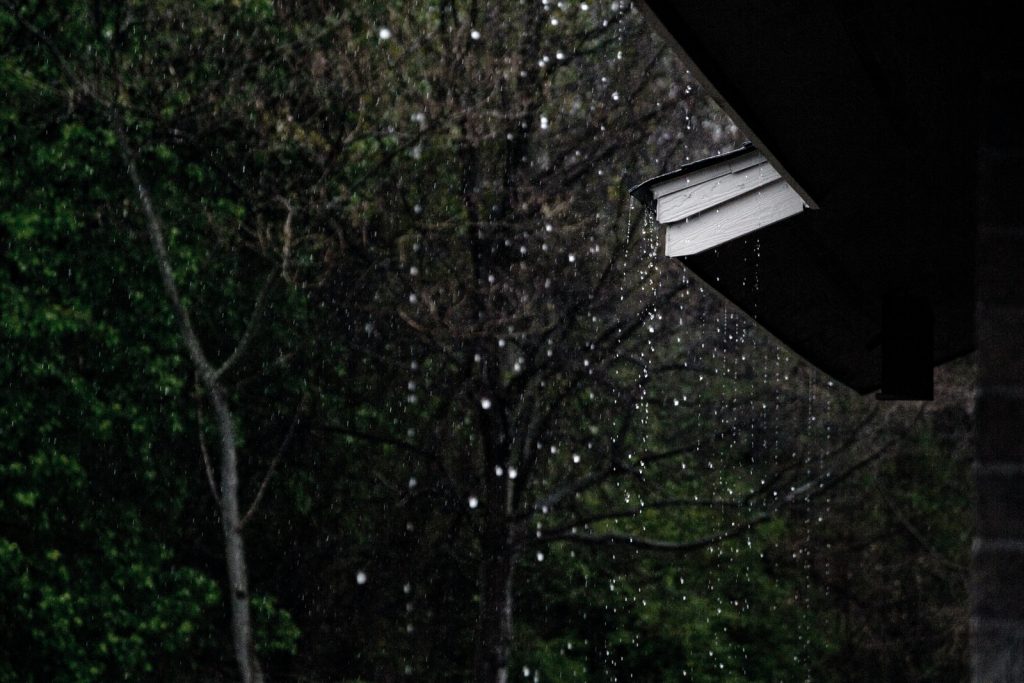Lluvia cayendo desde un techo con árboles de fondo