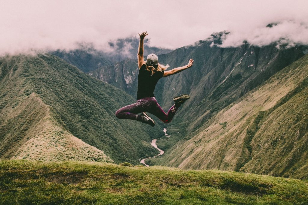 Mujer saltando en montaña con pastos verdes
