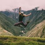 Mujer saltando en montaña con pastos verdes