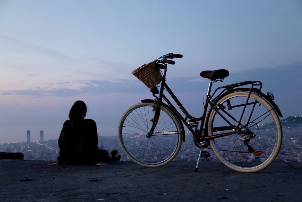 Persona sentada al lado de una bicicleta en montaña mirando ciudad