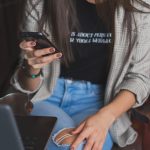 Mujer con jean y camisa sentada mirando el celular