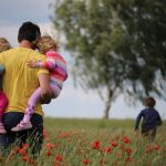 Hombre sosteniendo a dos niñas en campo con flores