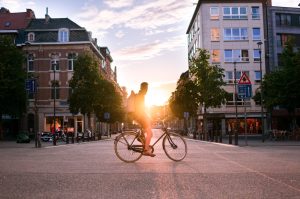 Hombre usando bicicleta en la ciudad con atardecer de fondo